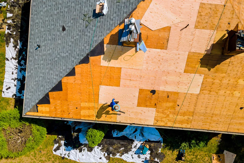 Roofer walking an exposed roof deck after a storm with the damaged shingles stripped away